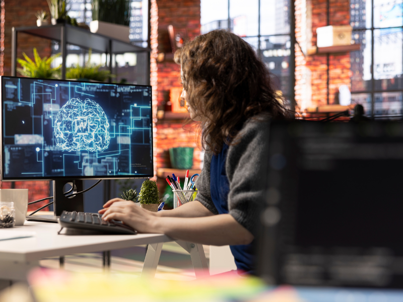A imagem mostra uma mulher trabalhando em um ambiente moderno e criativo, provavelmente um escritório de tecnologia, inovação ou startup.