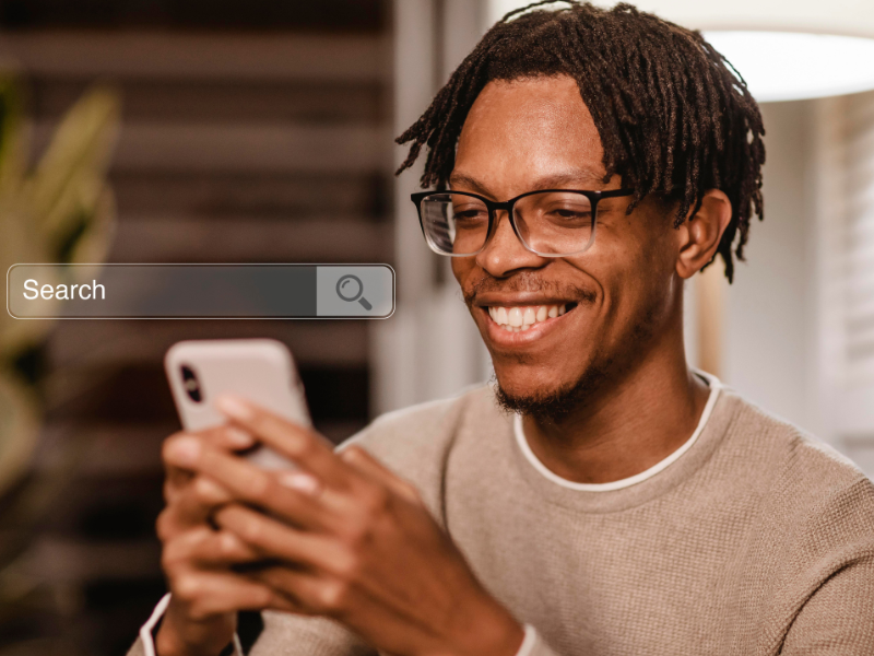 Descrição da Imagem
A imagem é um close-up de um jovem, focado em sua interação com um smartphone e sua expressão facial, com uma barra de pesquisa digital sobreposta.