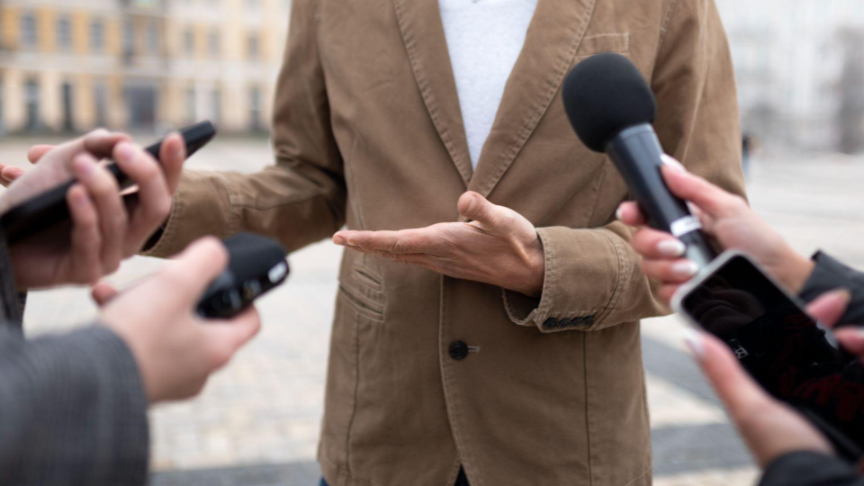 A imagem mostra uma entrevista à imprensa realizada em um ambiente externo.